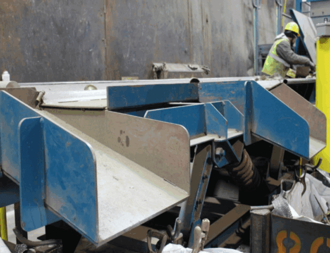 Close-up of metal recycling technology showing sorting equipment with a worker operating in the background.
