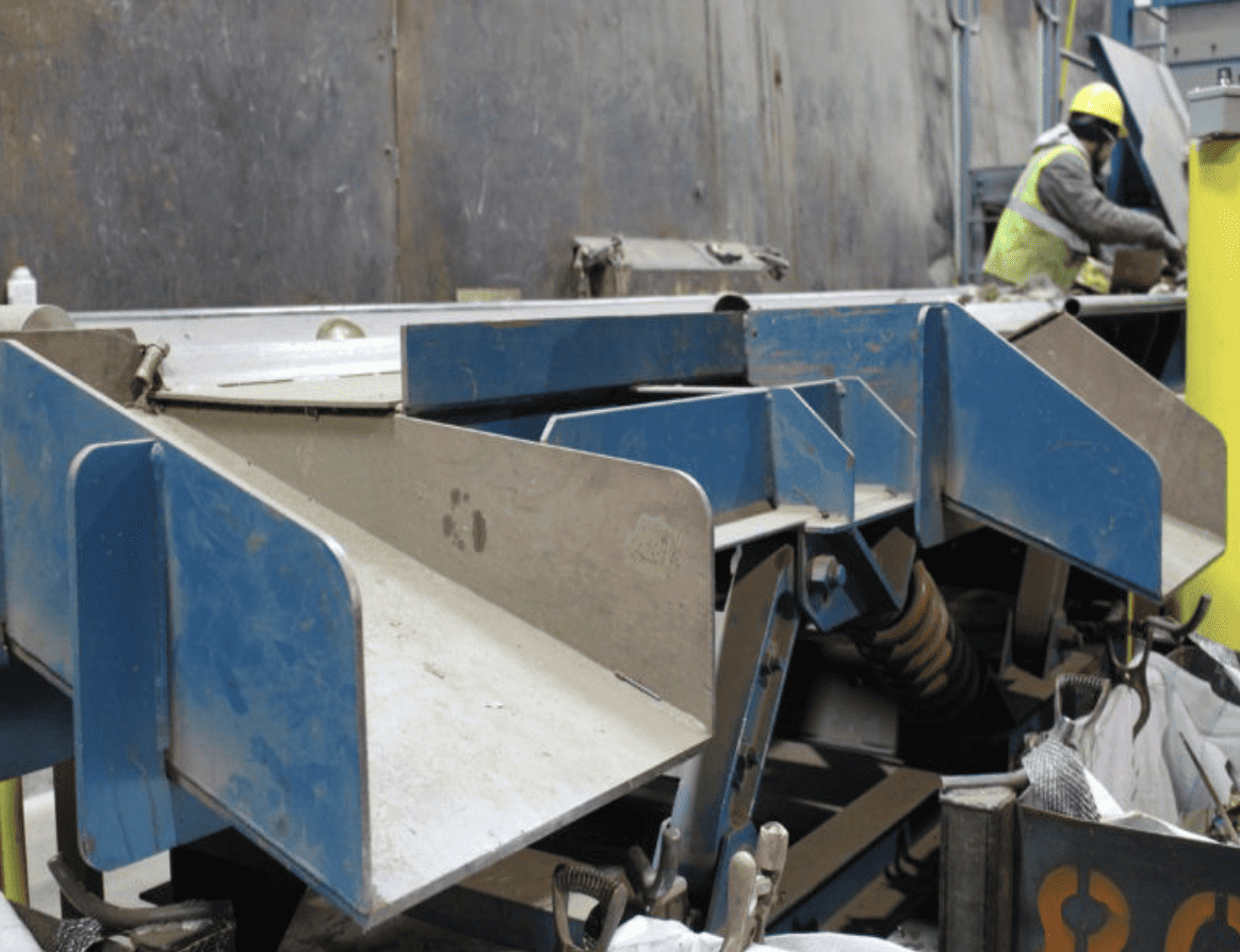 Close-up of metal recycling technology showing sorting equipment with a worker operating in the background.